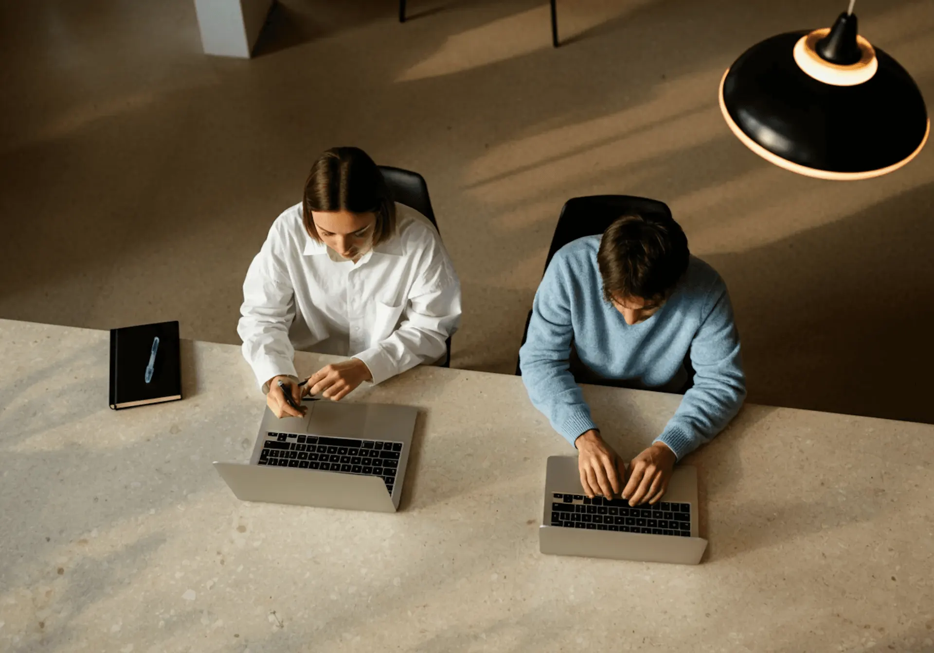 Man and woman working side by side at a desk, both focused on their laptops.