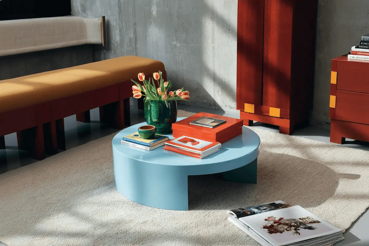 Modern interior space with a blue circular coffee table, flowers in a vase, and books neatly arranged.